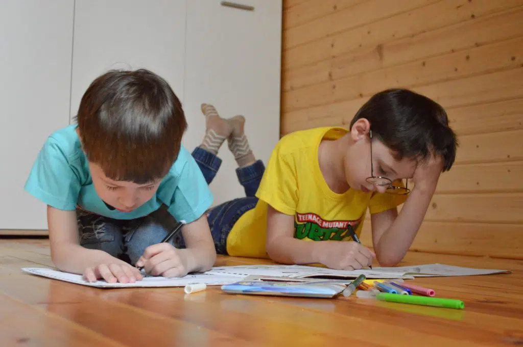 comment faire ses devoirs : deux enfants qui font leurs coloriages par terre 