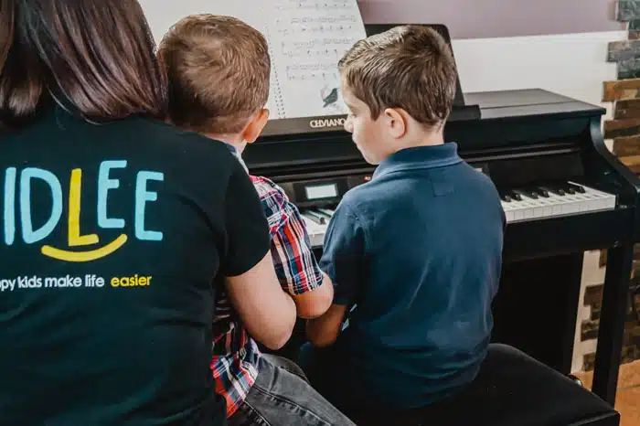 A nanny top Kidlee playing piano with the two little boys she's looking after 