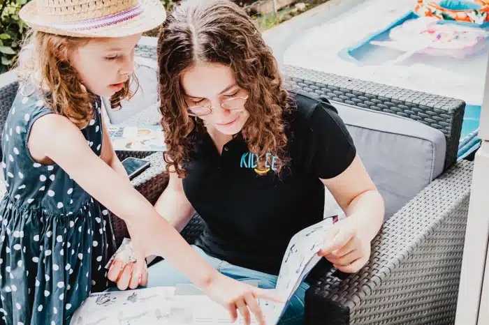 Recherche babysitter : une nounou top Kidlee avec la petite fille qu'elle garde en train de découvrir le contenu d'un livre ensemble 