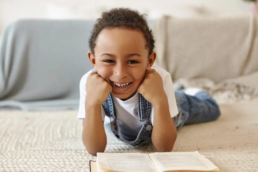Homework help: a child lying on the carpet and reading a book with a smile 