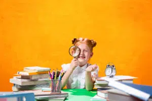 photo of a little girl looking through a magnifying glass and she is surrounded by books 