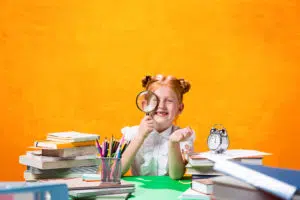 photo d'une petite fille qui regarde à travers une loupe et elle est entourée de livres 