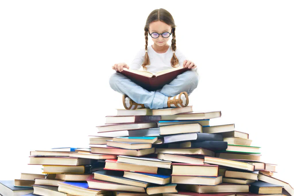 Portrait d'une petite fille avec un livre entre les mains et assise sur une montagne de livres 