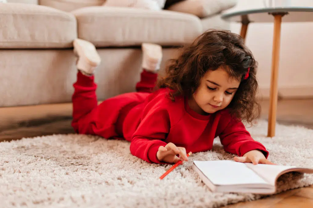 Petite fille allongé parre terre avec son crayon et son petit livre