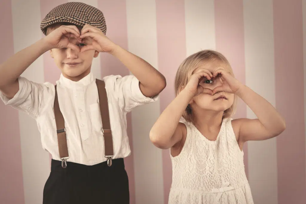 Une petite fille et un petit garçon en train de regarder à travers leurs doigts qui forment un coeur 