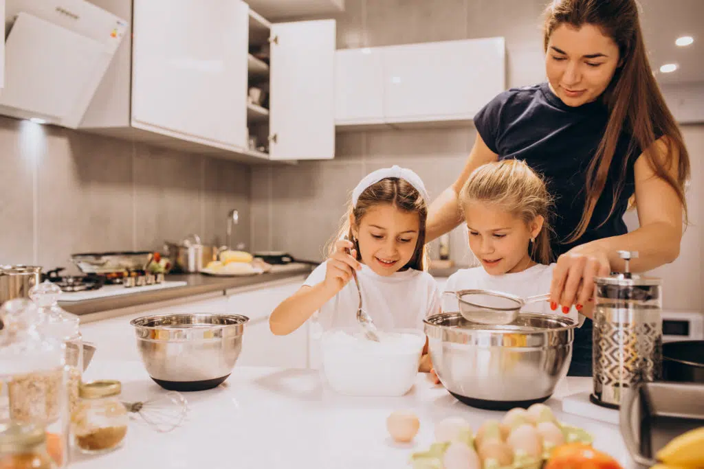garde d'enfant à domicile :  une babysitter en train de cuisiner avec les enfants qu'elle garde