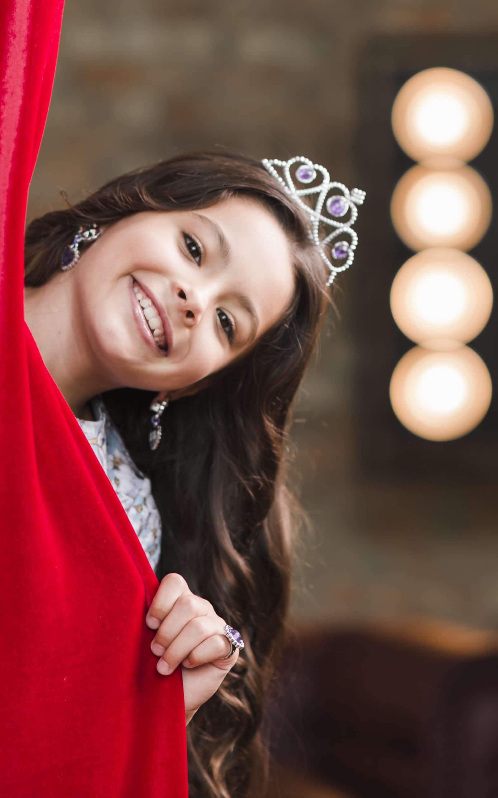 Théâtre enfants :Fille souriante avec une couronne sur Sa tête derrière rideau rouge