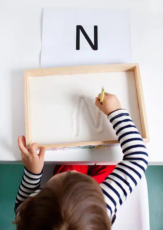 Activités à faire avec les enfants : un enfant en train d'écrire le lettre N dans un bac à sable