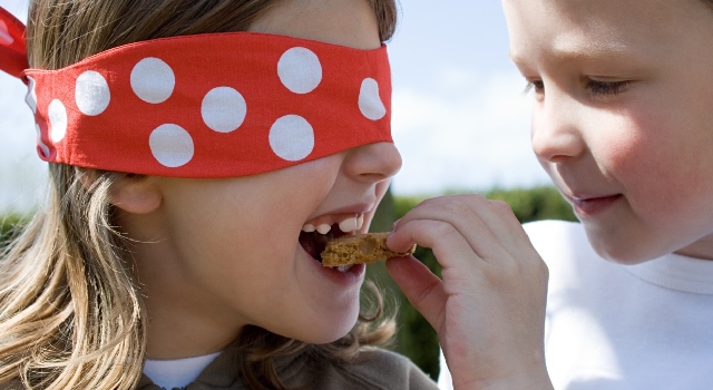 Un enfant qui fait goûter un cookie à sa soeur qui a les yeux fermés